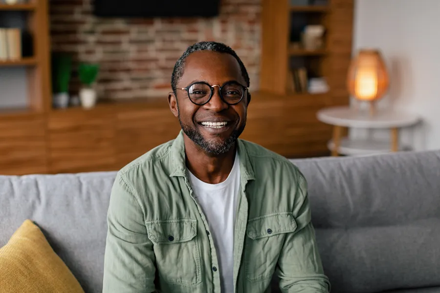 Andropause-Doctor A middle aged black man in a green button up shirt sits on his couch smiling, happy with his treatment for andropause and low testosterone from Delara Tavakoli, M.D. of Tavicare in Chevy Chase.