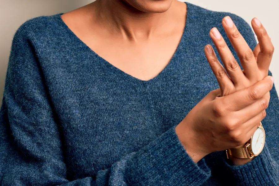 Arthritis-Doctor Close up of a woman in a blue sweater massaging one aching hand with the other. Get help for arthritis from Delara Tavakoli, M.D. of Tavicare in Chevy Chase.