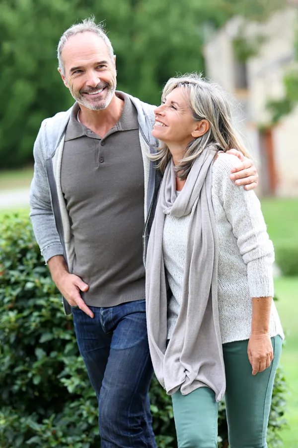 Bioidentical-Hormone-Therapy-Treatment A mature couple in gray toned clothes and jeans walk happily outside, happy with their successful bioidentical hormone treatments from Delara Tavakoli, M.D. of Tavicare in Chevy Chase.