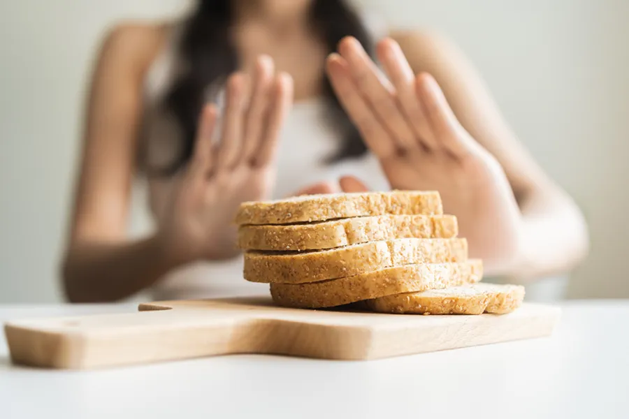 Celiac-Disease-Clinic Close up of a stack of bread slices on a cutting board with a woman's hands behind them, refusing to eat. Get treatment for Celiac Disease from Delara Tavakoli, M.D. of Tavicare in Chevy Chase.