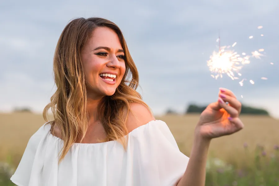 EMsella-for-Women-Clinic A cheerful young woman holding a lit sparkler in an open field at dusk satisfied with successful EMsella Pelvic Floor Strengthening treatment by Delara Tavakoli, M.D. of Tavicare in Chevy Chase.