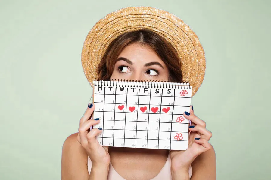 Menstrual-Dysfunction-Doctor A woman in a straw hat holds a calendar with several days marked off in front of her nose and mouth. Get treatment for menstrual dysfunction from Delara Tavakoli, M.D. of Tavicare in Chevy Chase.