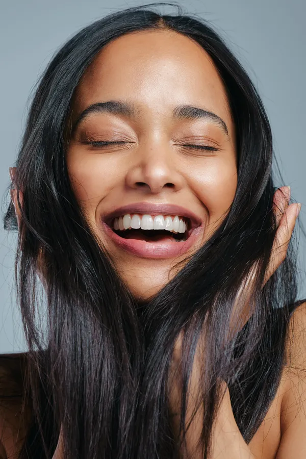PRP-for-Hair-Loss-Treatment A beautiful latin woman smiles and runs her fingers through her long, beautiful hair, happy with her PRP for hair loss and restoration treatment from Delara Tavakoli, M.D. of Tavicare in Chevy Chase.