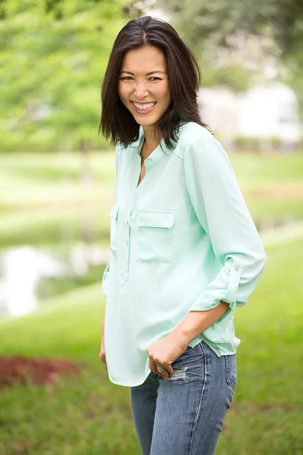 Perimenopause-Treatment A middle-aged brunette woman in a light green button-up shirt stands outside smiling, happy with her perimenopause treatment from Delara Tavakoli, M.D. of Tavicare in Chevy Chase.