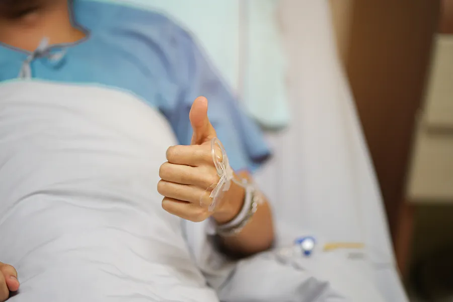 Post-Surgical-Recovery-Clinic A man recovering in a hospital bed gives the thumbs up. Schedule a post-sugical recovery IV drip from Delara Tavakoli, M.D. of Tavicare in Chevy Chase.