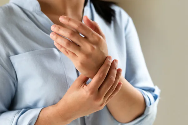 Rheumatoid-Arthritis-Clinic Close up of a woman in a blue blouse rubbing her wrist. Get rheumatoid arthritis treatment from Delara Tavakoli, M.D. of Tavicare in Chevy Chase.