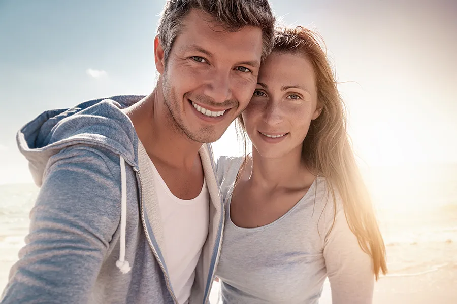 Skin-Conditions-Clinic A middle-aged couple stands on the beach with the sun behind them. Get treatment for medical skin conditions from Delara Tavakoli, M.D. of Tavicare in Chevy Chase.