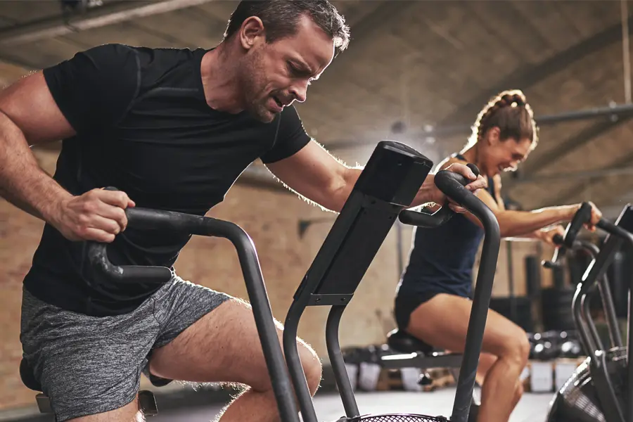 Tirzepatide-Doctor A couple in a brick gym work as hard as they can on exercise bikes, inspired by successful Tirzepatide treatment from Delara Tavakoli, M.D. of Tavicare in Chevy Chase.